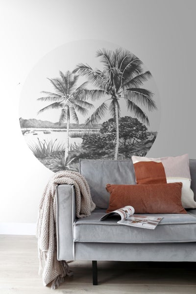 Wohnzimmer mit einer Fototapete mit Palmenmotiv hinter einem grauen Sofa.