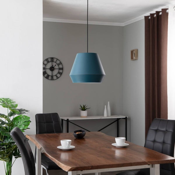 Modernes Esszimmer mit blauer Pendelleuchte über einem Massivholztisch und schwarzen Polsterstühlen in einem hellen Raum.