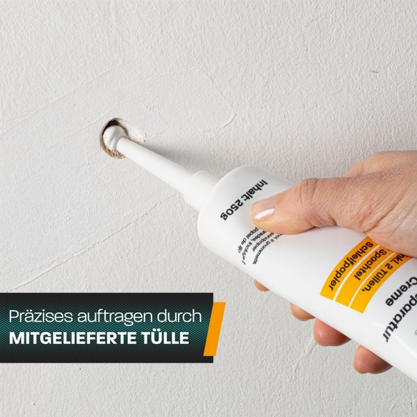 Eine Hand trägt Reparaturcreme mit einer Tülle aus einer Tube in ein Bohrloch in einer Wand auf.