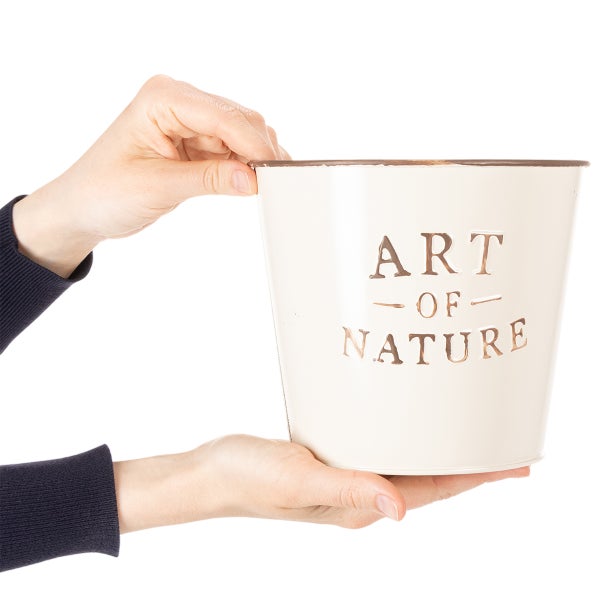 Eine Person hält einen hellen Blumentopf aus Metall mit der Aufschrift Art of Nature in den Händen.