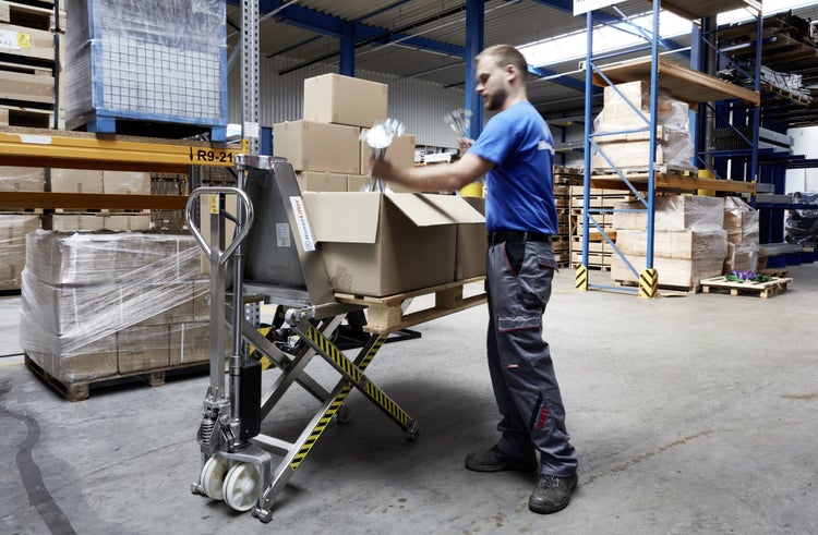 Mitarbeiter belädt Scherenhubwagen mit Kartons im Lager