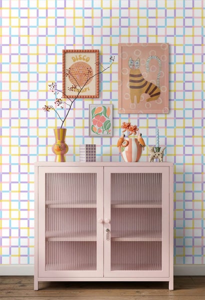 Hell gestalteter Wohnraum mit karierter Tapete, einem Sideboard mit geriffelten Glastüren und Dekorationsobjekten wie Vasen und Wandbildern.