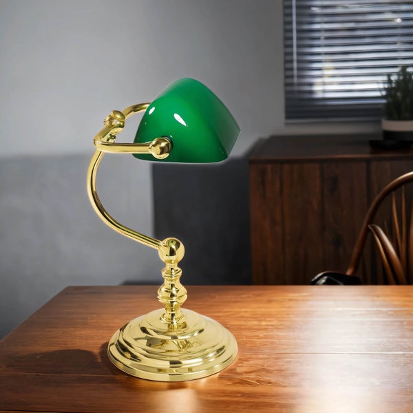 Tischleuchte mit grünem Schirm und goldenem Gestell auf einem Holztisch