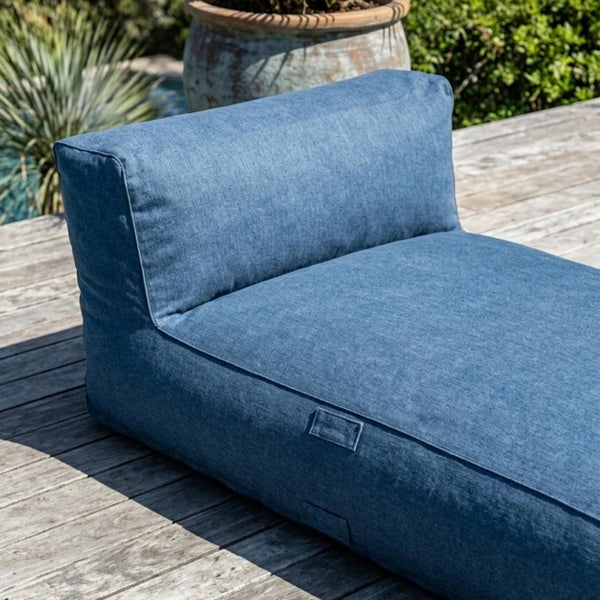 Blaues Outdoor-Loungekissen aus strukturiertem Stoff auf einer Holzterrasse.