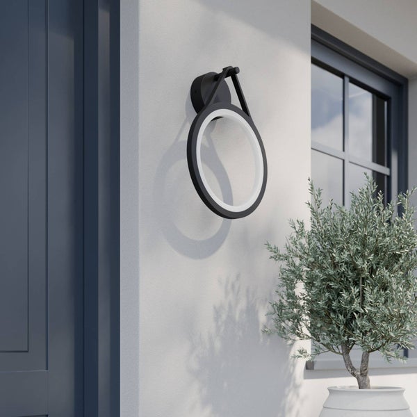 Moderne ringförmige LED Außenwandleuchte in Schwarz an einer Hauswand neben einer Tür und einem Fenster mit einer Topfpflanze.
