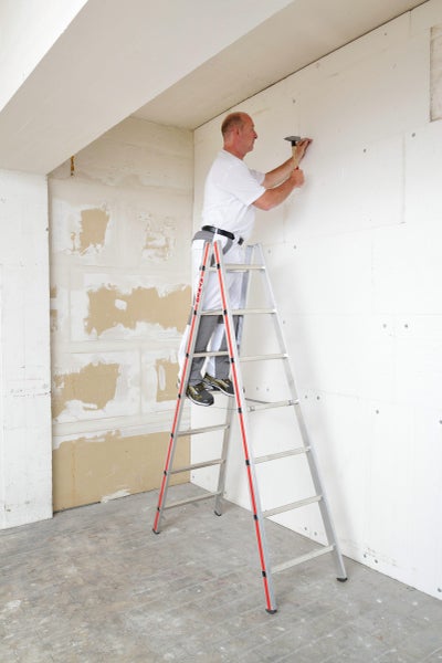 Handwerker auf Leiter befestigt Dämmplatten an Wand mit Hammer und Nagel.