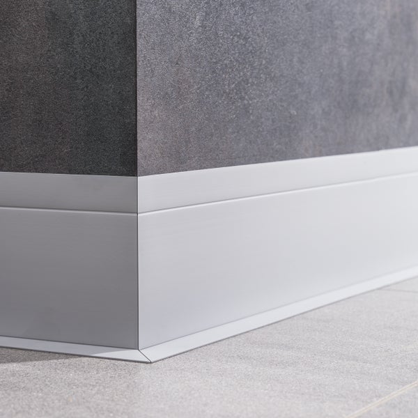 Sockelleiste aus Aluminium montiert an einer Wand mit dunklen Fliesen und einem Fliesenboden