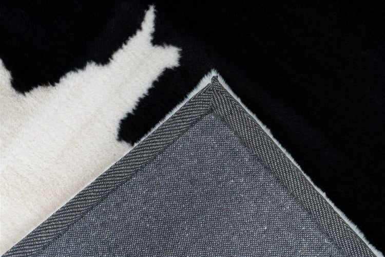 Nahaufnahme eines Teppichs in Kuhfell-Optik mit schwarz-weißem Muster und strukturierter Rückseite.