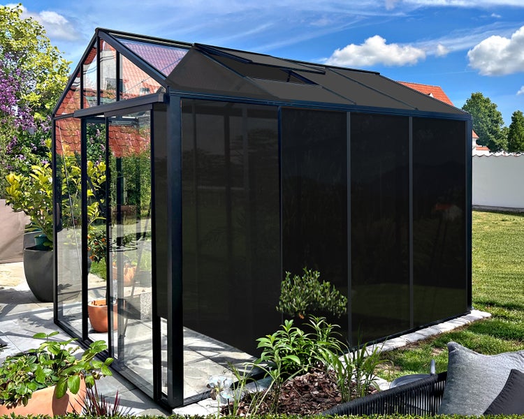 Freistehendes Gewächshaus mit schwarzem Aluminiumrahmen und dunklem Sonnenschutz an Dach und Seitenwänden in einem Garten.