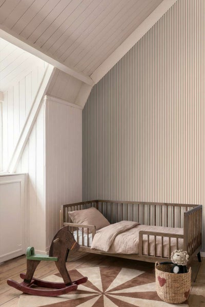Ein Kinderzimmer mit einer Tapete mit vertikalen Streifen, einem Holzbett, einem Schaukelpferd aus Holz und einem runden Teppich.