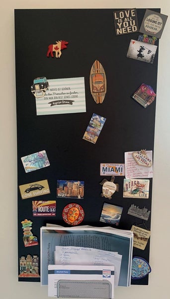 Schwarze Magnetwand mit verschiedenen Magneten, Postkarten und Notizzetteln an einer Wand.