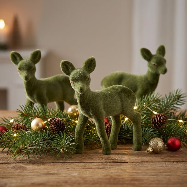Drei beflockte Rehfiguren als Weihnachtsdekoration auf einem Holztisch mit Tannenzweigen, Tannenzapfen und weihnachtlichen Kugeln.