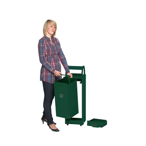 Eine Person setzt einen grünen Metallbehälter in ein passendes Metallgestell mit einer separaten Metallschale auf dem Boden.
