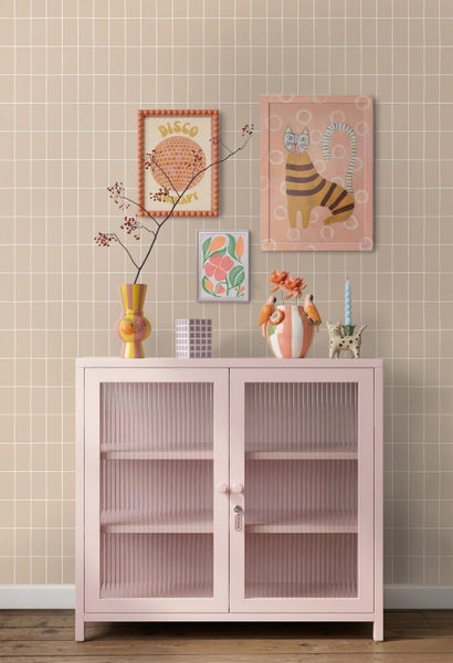Rosa Vitrine mit geriffelten Glastüren vor einer gefliesten Wand, dekoriert mit Vasen und gerahmten Wandbildern.