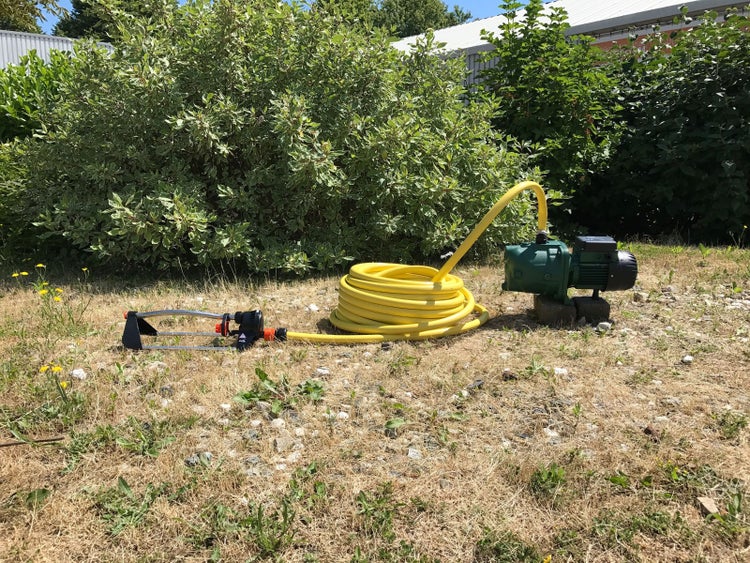 Grüne Gartenpumpe mit angeschlossenem gelbem Gartenschlauch im Außenbereich.