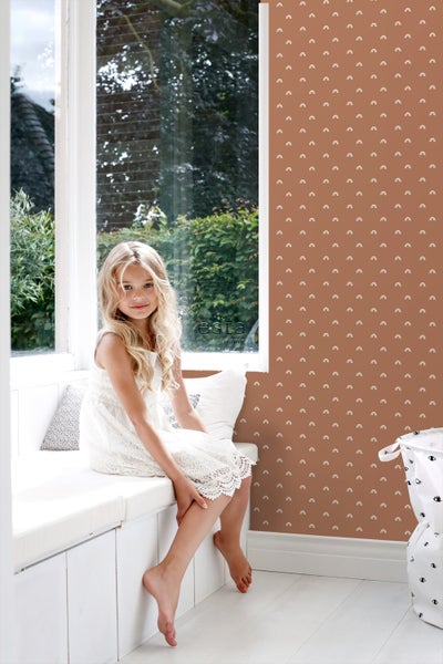 Helles Zimmer mit einem Mädchen am Fenster und einer Wand mit Regenbogenmuster.