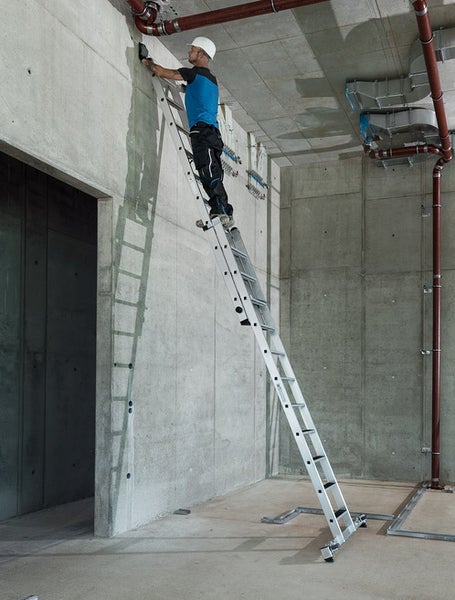 Handwerker auf einer Mehrzweckleiter bei Installationsarbeiten in einem Rohbau.