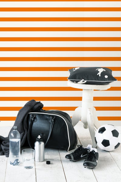 Szene mit Sporttasche, Fußball, Fußballschuhen, Trinkflasche und Kissen auf einem Hocker