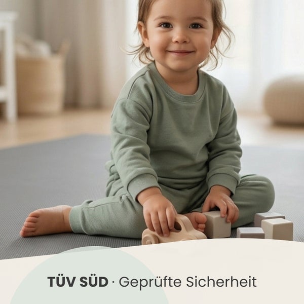 TÜV SÜD Geprüfte Sicherheit Zertifizierung. Ein Kind spielt mit Holzspielzeug auf einer grauen Spielmatte.