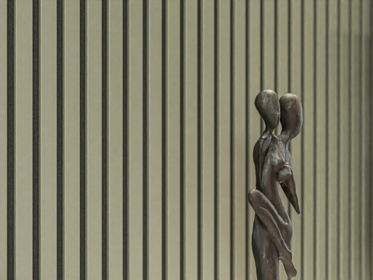 Dekorative Skulptur eines menschlichen Paares vor einer modernen Wandverkleidung mit Lamellenoptik