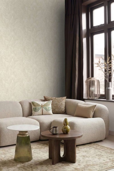 Wohnzimmer mit Vliestapete mit Palmenblattmuster, modernem Sofa, zwei Couchtischen und Fenster mit Vorhängen in wohnlichem Ambiente.