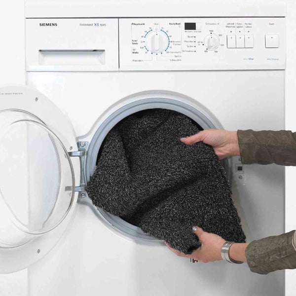 Eine Person legt eine Fußmatte in eine Siemens Waschmaschine
