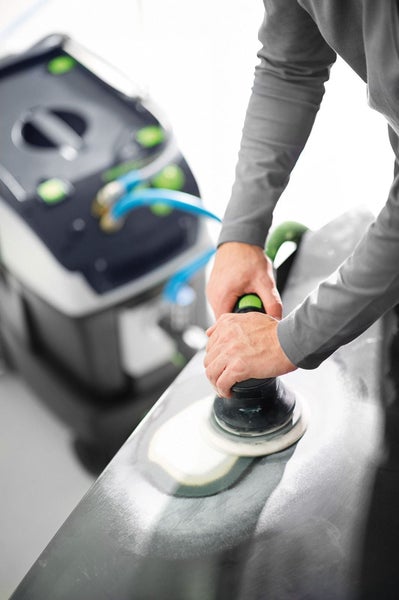 Mann schleift eine Oberfläche mit einem Exzenterschleifer, im Hintergrund ein Absauggerät.