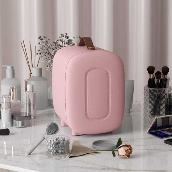 Rosa Kosmetikkühlschrank im modernen Design auf einem hellen Marmorschminktisch, organisiert mit Hautpflegeprodukten und Make-up-Zubehör.