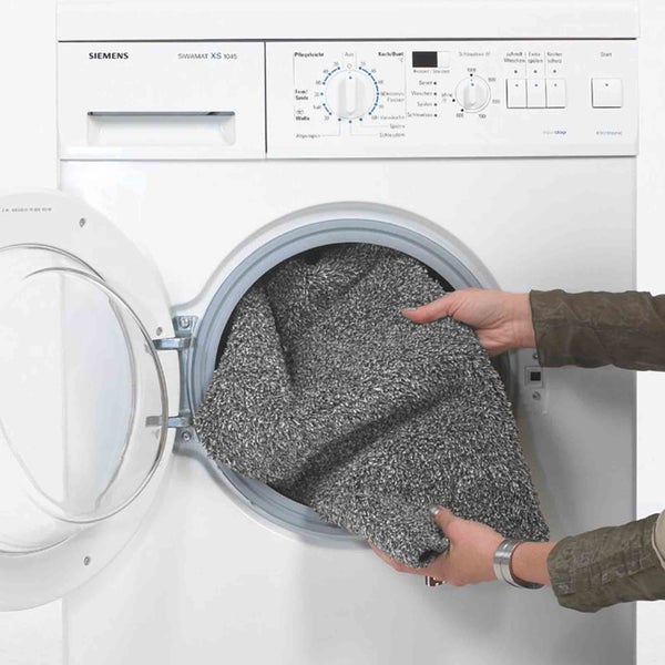 Eine Person legt eine graue, flauschige Badematte in eine Waschmaschine von Siemens.