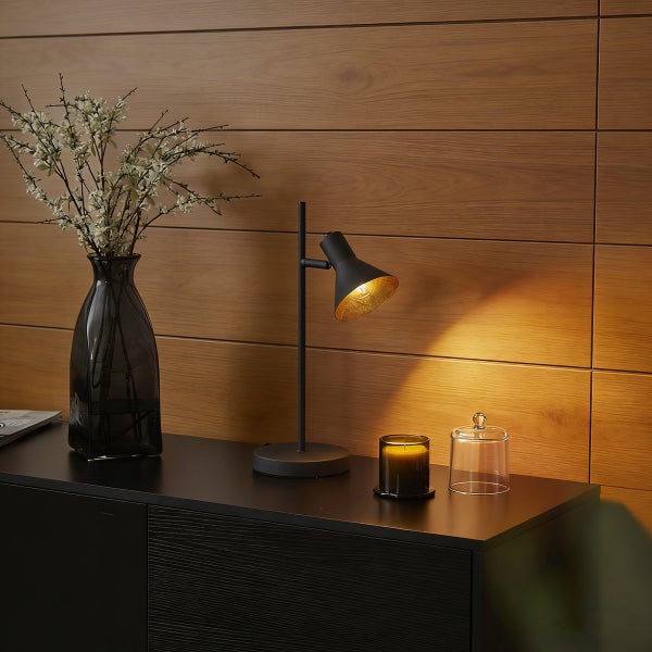 Dekorative Tischleuchte, Vase, Duftkerze und Glasglocke auf schwarzem Sideboard vor Holzwand