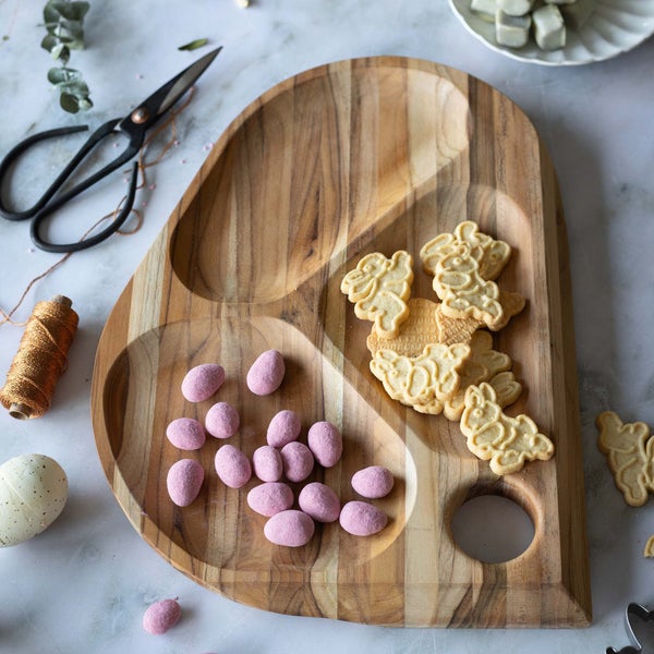 Dekorative Holzplatte mit Süßigkeiten, Osterkeksen, Schere und Garn