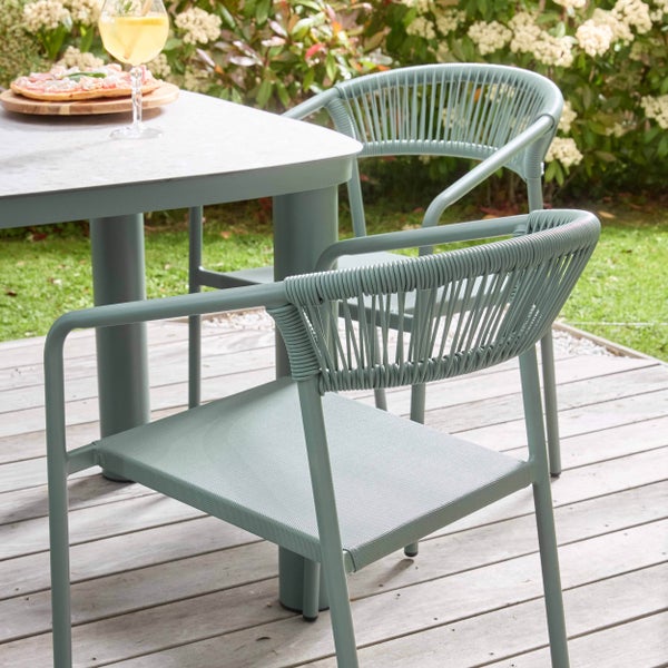 Gartenset aus zwei stapelbaren Stühlen mit Seilbespannung und einem Esstisch auf einer Holzterrasse im hellen Garten.