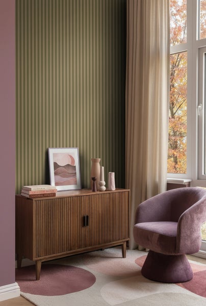 Gestreifte Tapete an einer Wand hinter einem hölzernen Sideboard in einem modern gestalteten Wohnzimmer mit Sessel und Teppich.