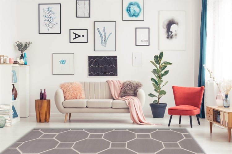 Wohnzimmer mit modernem Sofa, rotem Sessel und geometrisch gemustertem Teppich vor einer Bilderwand.