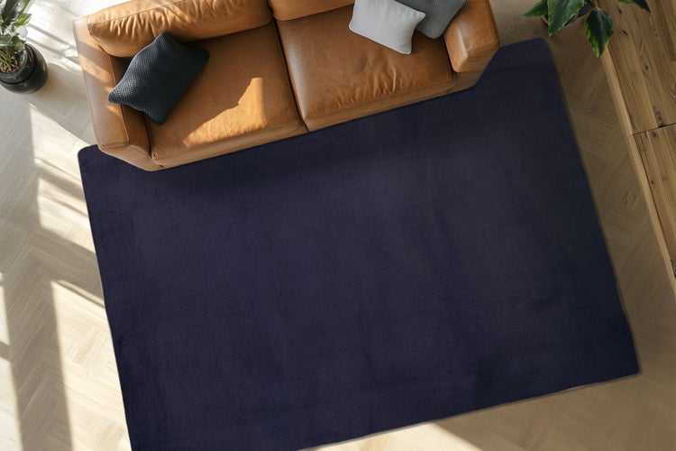 Dunkelblauer Wohnzimmerteppich in rechteckiger Form vor einem Ledersofa auf einem Holzboden in einem modernen Wohnbereich.