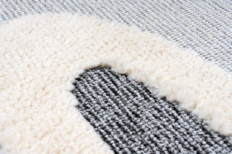 Detailansicht eines Teppichs mit strukturierter Weboptik und erhabenem, weichem Flor in Bogenform.