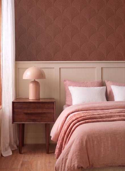 Schlafzimmer-Einrichtung mit einem Bett mit rosafarbener Bettwäsche, einem Nachttisch aus dunklem Holz und einer strukturierten Tapete mit Bogenmuster.