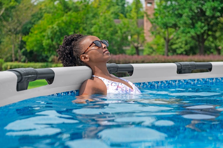 Eine Person mit Sonnenbrille lehnt am weißen Rand eines Aufstellpools im Garten.