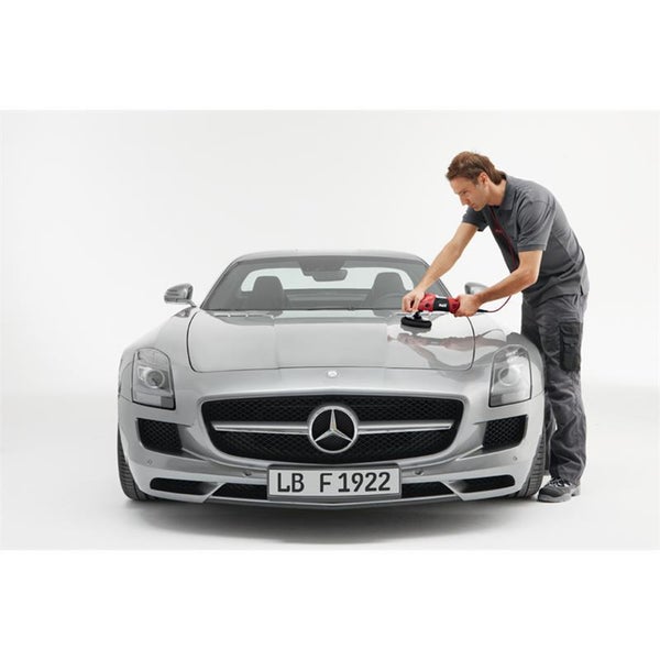 Ein Arbeiter poliert die Motorhaube eines silbernen Sportwagens mit einer elektrischen Poliermaschine.