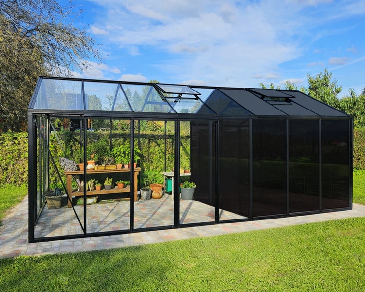 Großes Gewächshaus mit schwarzem Metallrahmen, halb transparent und halb getönt, mit Pflanztisch und Töpfen auf Pflaster im Garten.