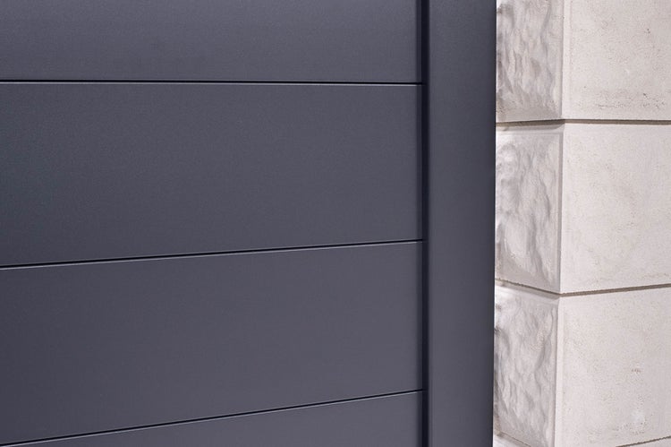 Anthrazitfarbenes Zaunelement mit horizontalen Lamellen und Pfosten neben einer strukturierten Steinmauer.