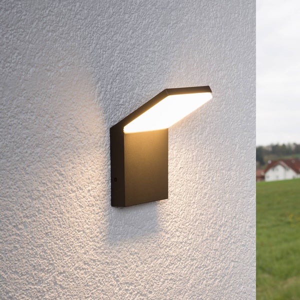 Moderne schwarze LED-Außenwandleuchte an einer weißen strukturierten Wand mit warmweißem Lichtschein.