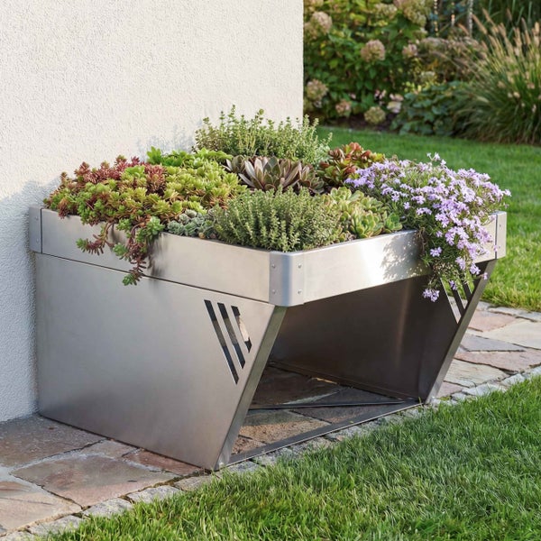 Mähroboter-Garage aus Metall mit integriertem Pflanzkasten, bepflanzt mit Sukkulenten und Blumen, im Garten an einer Hauswand.