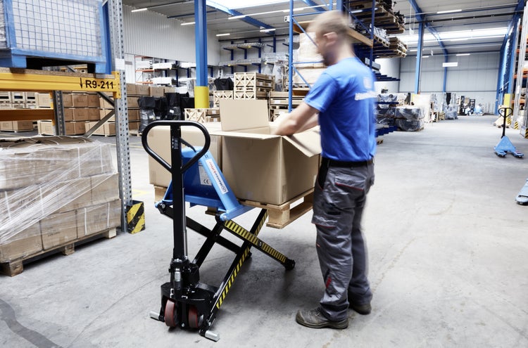 Ein Mitarbeiter packt Kartons auf einen Hubtischwagen in einem Lager.