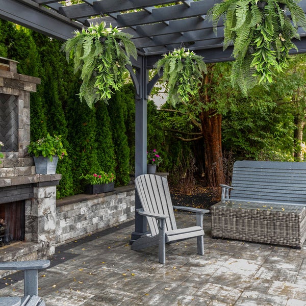 Moderne Terrasse mit grauer Pergola, hängenden Kunstfarnen, grauem Adirondack-Stuhl und Gartenbank. Steinpflasterboden. Organisiert und hell.