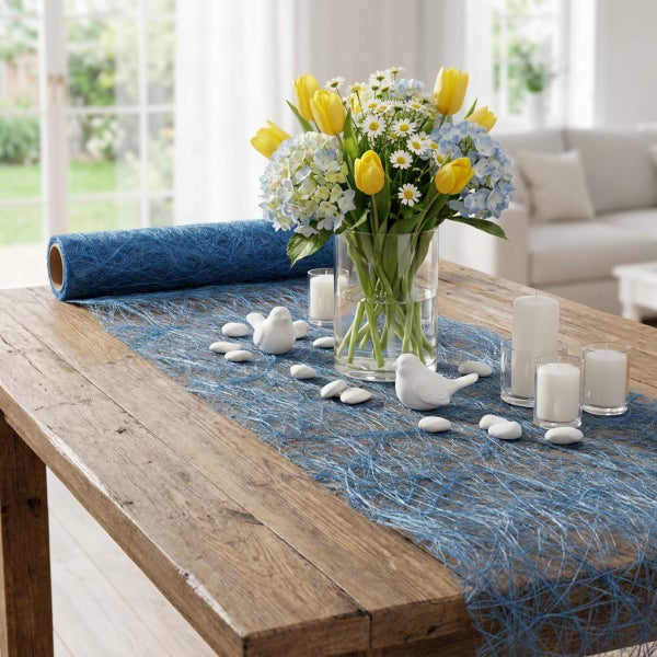 Tischdekoration mit blauem Sisal Tischband, Glasvase mit Frühlingsblumen, weißen Kerzen und dekorativen Vögeln auf einem Holztisch.