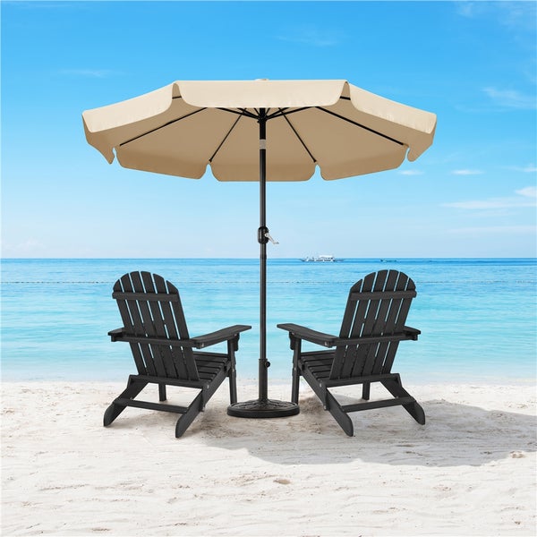 Zwei schwarze Adirondack Stühle unter einem Sonnenschirm am Strand.