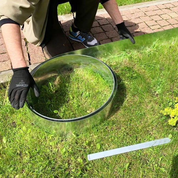 Person installiert eine Rasenkante aus Metall im Garten.
