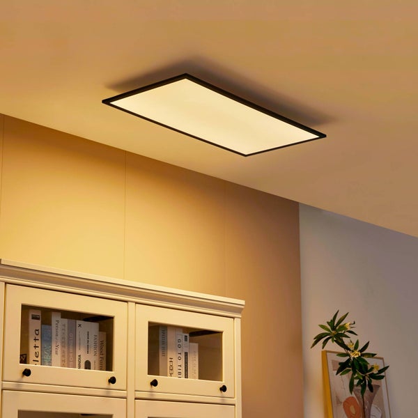 Rechteckige LED-Deckenleuchte mit schwarzem Rahmen in einem hellen Raum über einem weißen Bücherschrank.