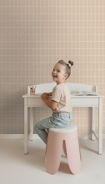 Mädchen sitzt an einem Schreibtisch vor einer Wand mit Kachelmuster.